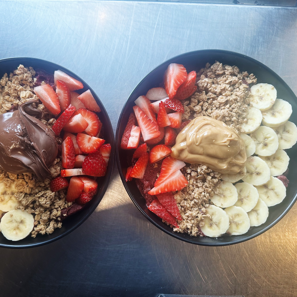 Two smoothie bowls with granola, strawberries, bananas, and a dollop of Nutella or peanut butter.