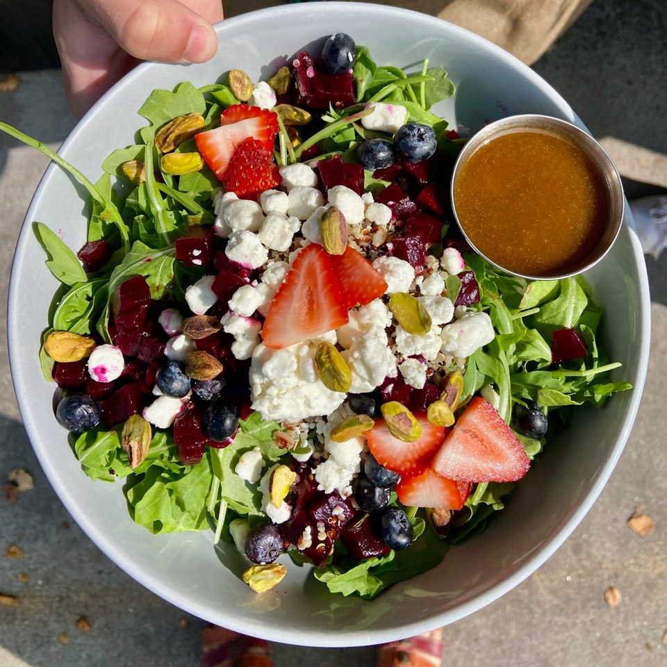A vibrant salad with arugula, beets, blueberries, strawberries, goat cheese, pistachios, and dressing.