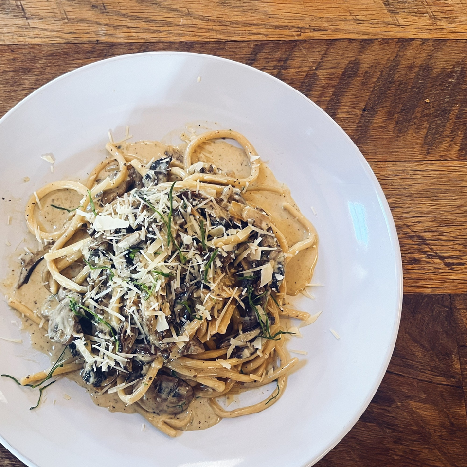 Creamy mushroom pasta with grated cheese and herbs on a white plate, on a wooden table.