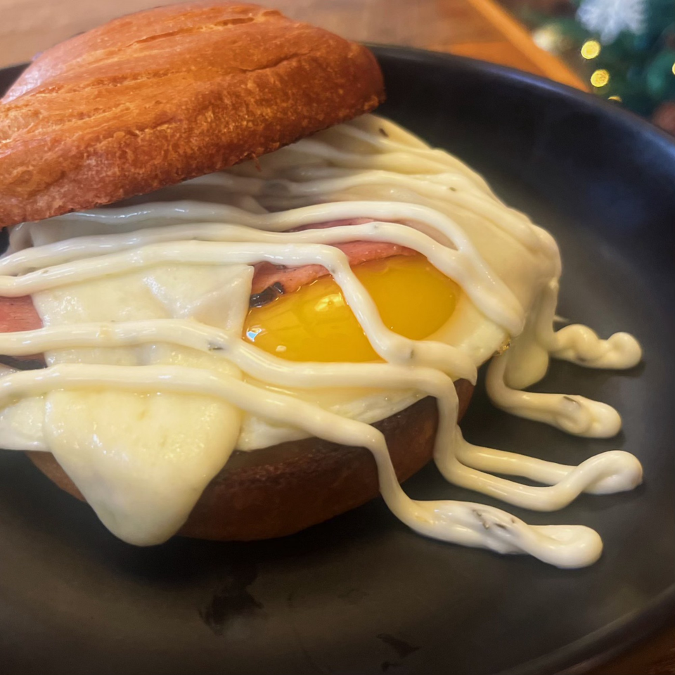 A breakfast sandwich with a fried egg, bacon, and melted cheese on a bun, served on a black plate.