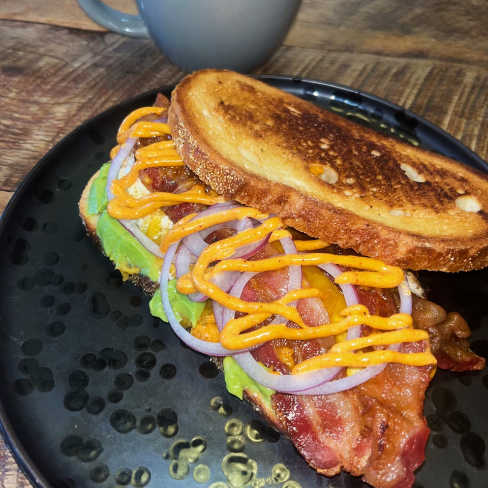Tavern on 28's open-faced sandwich with bacon, avocado, red onion, and sauce on toasted bread.