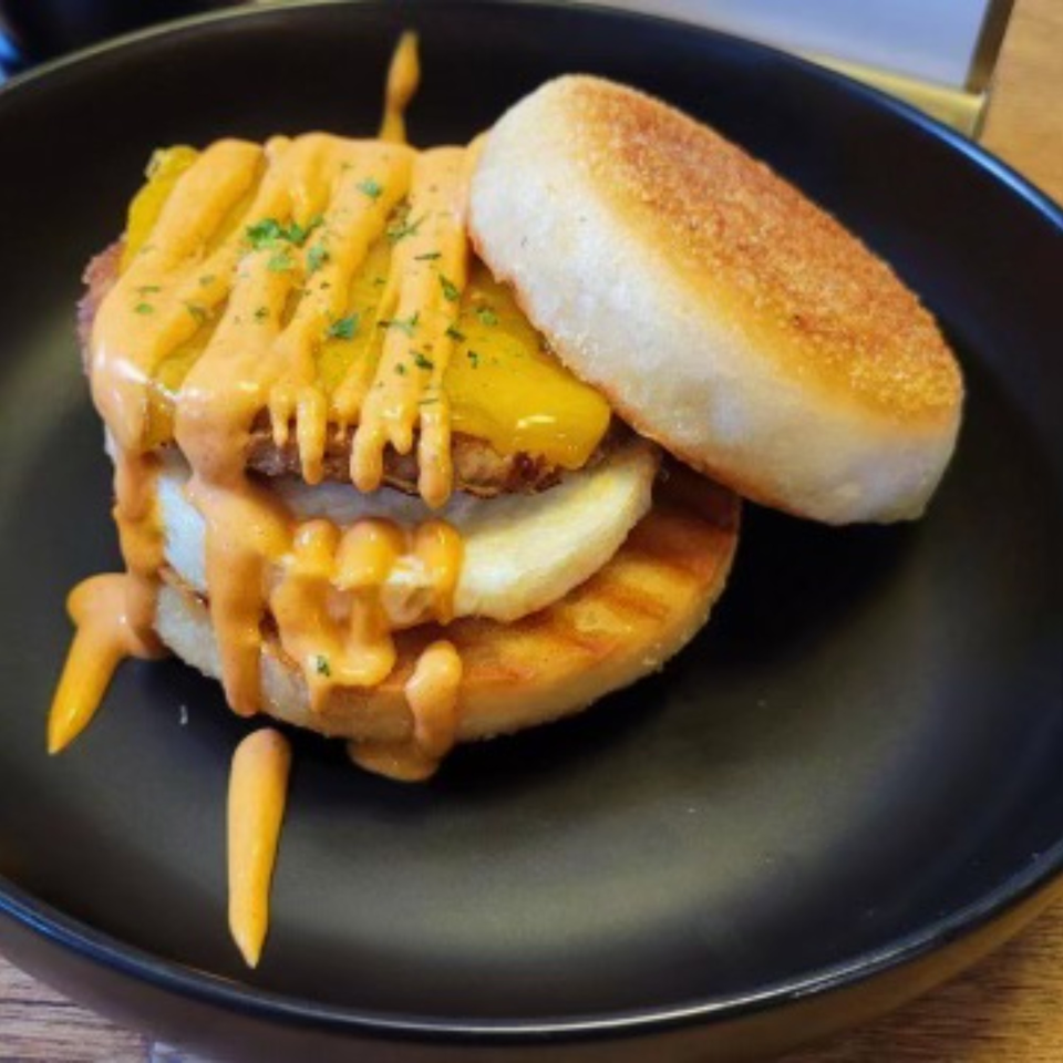 Breakfast sandwich with egg, cheese, and sauce on an English muffin, served on a black plate.