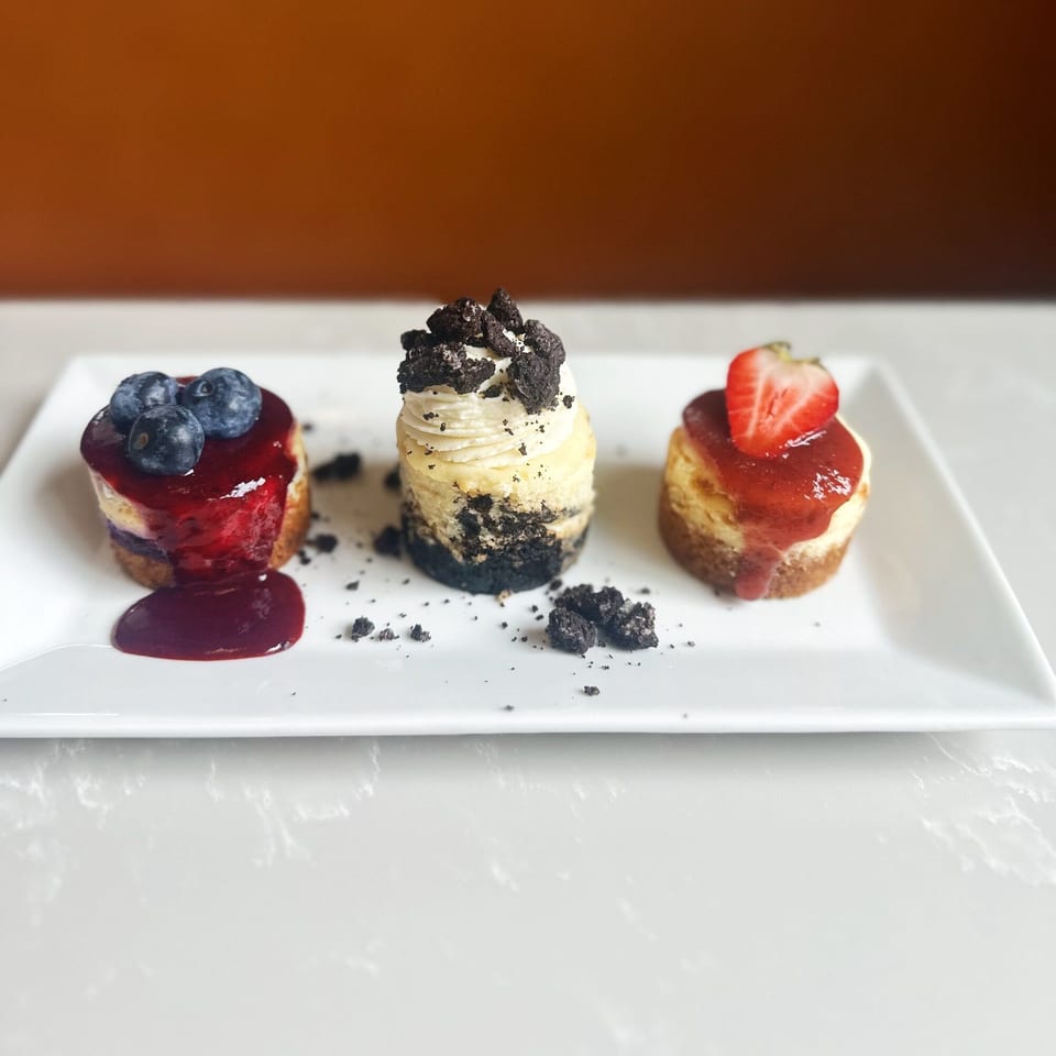 Three mini cheesecakes, one with blueberries, one with Oreo crumbles, and one with a strawberry.