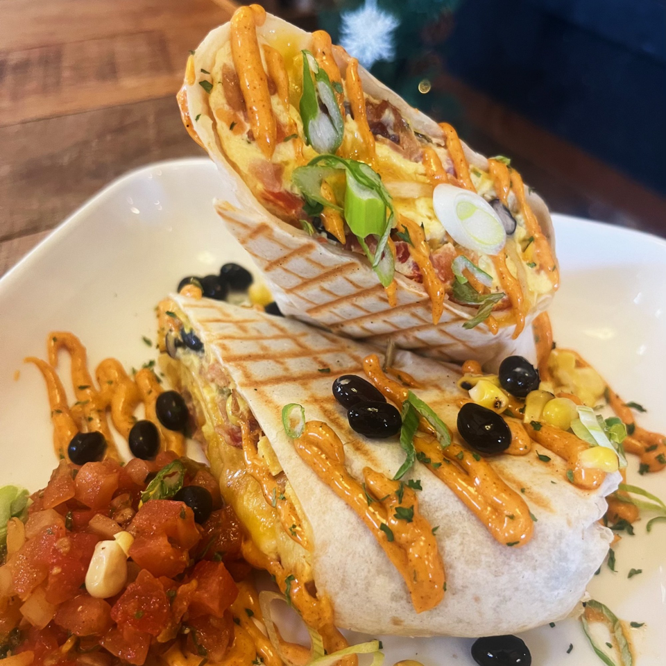 Two grilled breakfast burritos with orange sauce, black olives, corn, and a side of salsa.